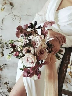 a woman holding a bouquet of flowers in her hand and sitting on a wooden chair