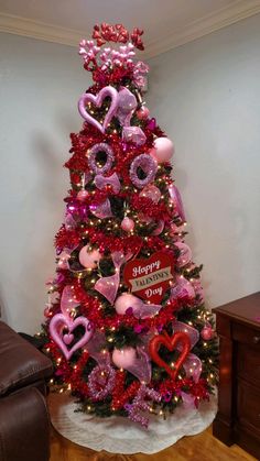 a decorated christmas tree with pink and red hearts on it's top, in the corner of a room