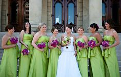 a group of women standing next to each other in front of a building holding bouquets