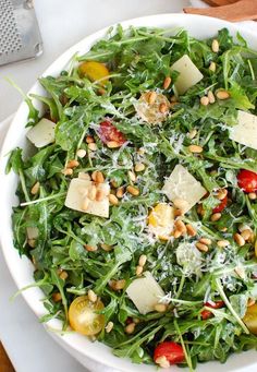 a salad with cheese, tomatoes and pine nuts in a white bowl on a table