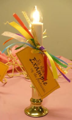 a lit candle on top of a pink table cloth with ribbons and tags attached to it