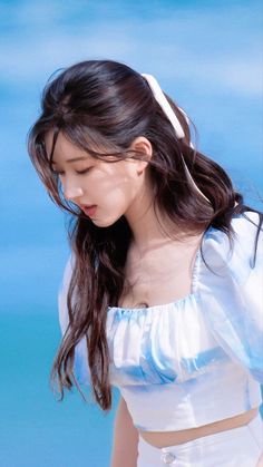 a woman with long dark hair wearing a white and blue top standing on the beach