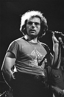 an old photo of a man with glasses on holding a microphone in front of him