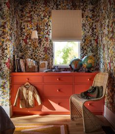 an orange dresser and chair in a room with floral wallpaper