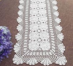 a white lace table runner next to purple flowers