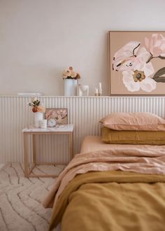 a bed sitting next to a table with flowers on it and a painting above it