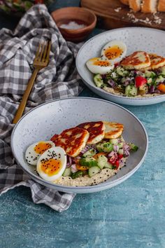 two bowls filled with food sitting on top of a blue counter next to a knife and fork