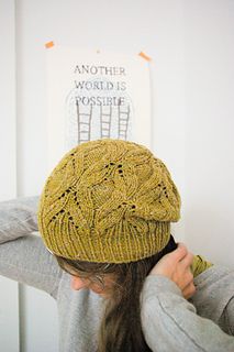 a woman wearing a yellow knitted hat while standing next to a white wall and holding her hair in one hand