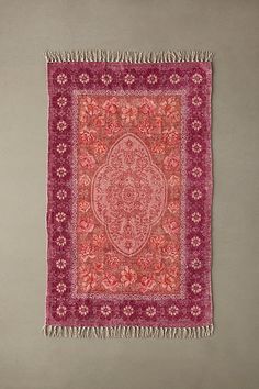 a red and pink rug with fringes hanging on the wall in front of a gray wall