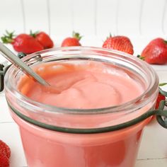 a jar filled with pink liquid next to strawberries on a white counter top and two spoons in the jar