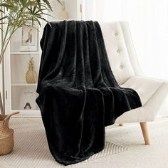 a black blanket sitting on top of a white chair next to a potted plant