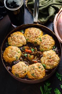 a pan filled with meat patties next to a glass of beer