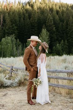 a bride and groom standing in front of a wooden fence with trees in the background