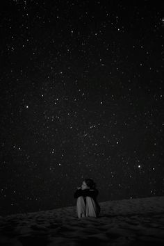 two people sitting in the sand looking up at the stars