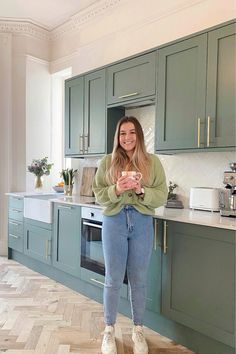 a woman standing in the middle of a kitchen with green cabinets and white counter tops