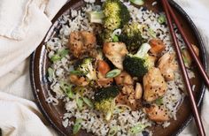 a plate with rice, broccoli and chicken on it next to chopsticks