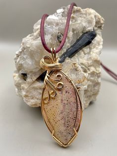 "I wire wrapped this beautiful colorful natural Banana skin fossil in 14k Gold fill wire.  It is shades of yellow & rose pink with burgundy.  It measures 2 1/8\" x 7/8\" and is hung on a 26\" dark burgundy violet leather cord to compliment the pendant colors. Hand formed hook closure.  This is truly unique and one of a kind! Looking closely, you can see the agatized sections in the banana skin.   Handcrafted Artisan Jewelry. Made in the USA with love.  Each piece ships in a gift box. Each of the Hand Wrapped Gold Agate Necklaces, Hand Wrapped Gold Agate Necklace, Unique Hand Wrapped Oval Pendant Jewelry, Artisan Freeform Gold Jewelry, Unique Freeform Gold Necklace, Unique Yellow Gold Wire Wrapped Necklaces, Nature-inspired Gold Wire Wrapped Jewelry, Gold Hand Wrapped Nature-inspired Jewelry, Unique Yellow Gold Wire Wrapped Necklace