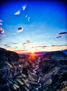 the sun is setting over a canyon with mountains in the foreground and water running through it