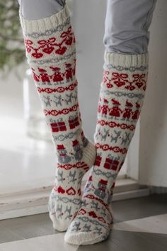 the legs of a woman wearing socks with red and gray designs on them, standing in front of a window