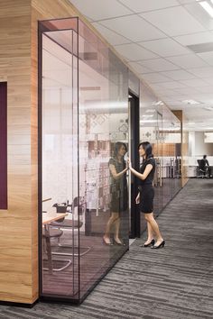 two women are standing in an office with glass partitions on either side of them