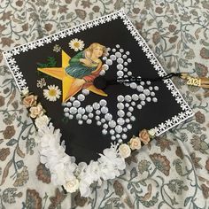 a graduation cap decorated with flowers and an angel on it is laying on a bed