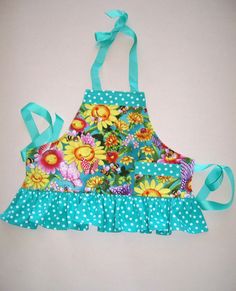 a blue apron with flowers and polka dots on the bottom is hanging from a green ribbon