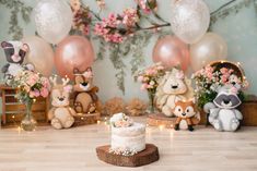 a cake sitting on top of a wooden table next to stuffed animals and balloons in the background