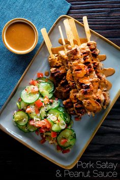 grilled chicken skewers and cucumber salad on a plate with dipping sauce