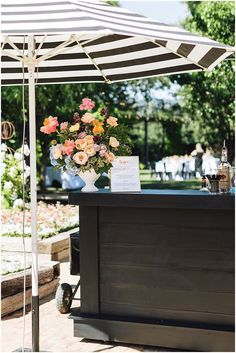 an outdoor bar with flowers and drinks on the table under an open umbrella for shade