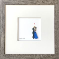 a white frame with a blue and grey figurine holding a red heart in it