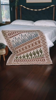 a bed sitting on top of a wooden floor next to a night stand with a blanket over it