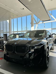 a black car is parked in a showroom with other cars on the floor and large windows