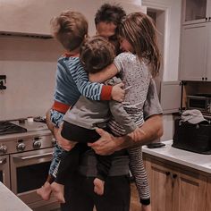 a man holding two children while standing in a kitchen next to a stove top oven