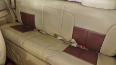 the interior of a car with beige and brown leather seats, one has a seat belt on it