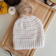 a white knitted hat sitting on top of a cutting board next to some yarn