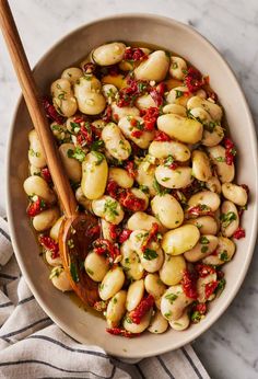 a white bowl filled with beans and garnished with herbs next to a wooden spoon