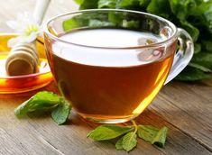 a glass cup filled with green tea next to some leaves and honey on a wooden table