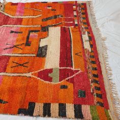 an orange and red rug with fringes on it sitting on top of a bed