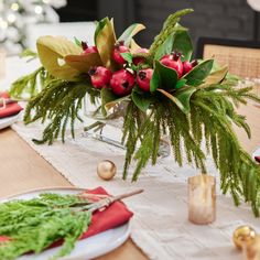 the table is set for christmas dinner with red flowers and greenery in glass vases