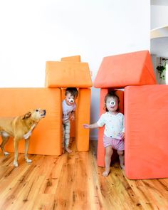 two small children playing in an orange play house with a dog standing next to it