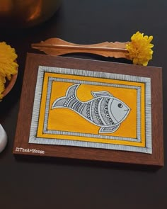 a wooden frame with a fish on it next to flowers and a vase filled with yellow dandelions