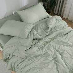 an unmade bed with green sheets and pillows on the floor next to a potted plant