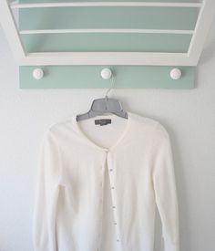 a white cardigan hanging on a green and white coat rack next to a wall