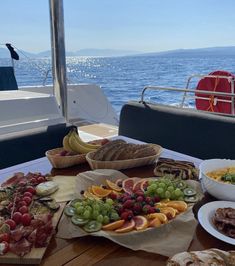 a wooden table topped with plates and bowls filled with food on top of it next to the ocean