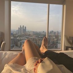 a woman laying on top of a bed in front of a window next to a tall building