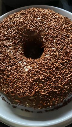 a chocolate frosted donut sitting on top of a white cake plate covered in sprinkles