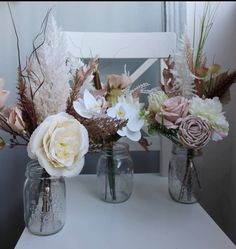 three vases filled with flowers sitting on top of a white table next to a mirror