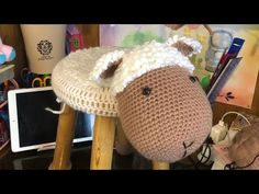 a crocheted sheep sitting on top of a wooden stool next to a tablet