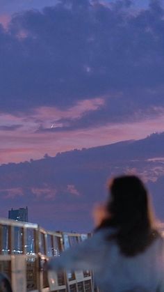 a woman is flying a kite on the roof of a building at dusk with clouds in the background