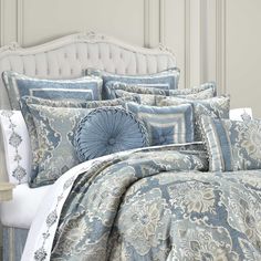 a bed with blue and white comforters on top of it in front of a headboard